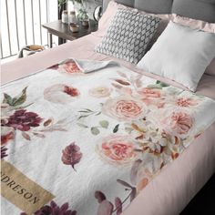 a bed with pink and white flowers on it, along with two pillows in the background