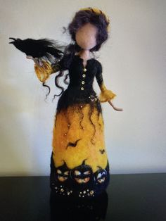 a doll dressed in black and yellow with a bird on her arm, sitting on a table