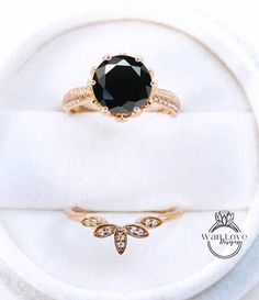 a black diamond ring sitting on top of a white velvet covered cushioned surface next to an engagement ring