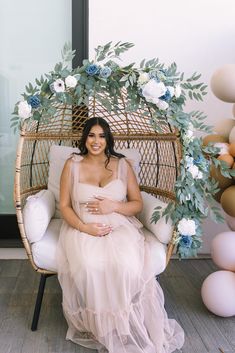 a pregnant woman sitting in a wicker chair with flowers and balloons around her head