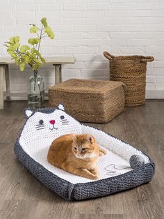 an orange and white cat laying on top of a pet bed next to a plant