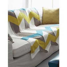 a white couch sitting next to a window with yellow and blue pillows on top of it