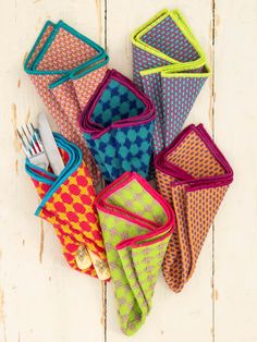 six colorful napkins with forks in them on a white wooden surface, next to a knife and fork