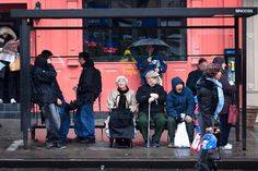 a group of people standing on the side of a train track next to a red building