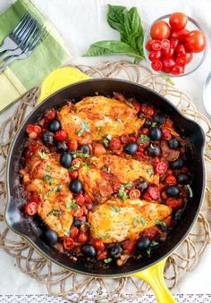 a skillet filled with chicken, tomatoes and olives on top of a table