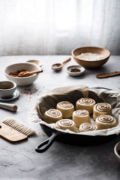 a pan filled with rolls next to bowls and spoons on top of a table