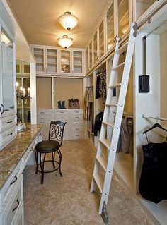 a ladder is in the middle of a walk - in closet with white cabinets and drawers