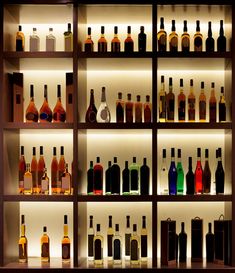 bottles of alcohol on shelves in a liquor store or bar, with lighting behind them