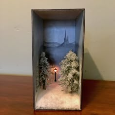 an open box with trees and a street light in the snow on a wooden table