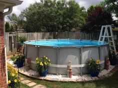 an above ground swimming pool surrounded by flowers and plants in a backyard with a ladder to the side