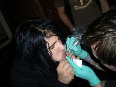 a woman getting her teeth brushed by a man with blue gloves and rubber gloves on