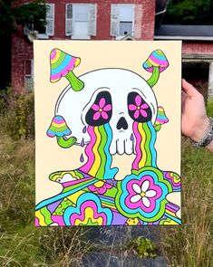 a person holding up a painting with a skull on it in front of a building