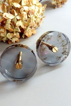 two glass knobs with gold flowers on them sitting on a table next to a pine cone