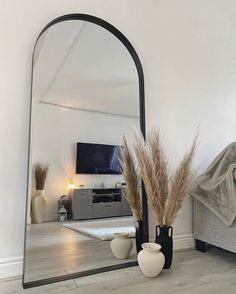 a mirror sitting on top of a wooden floor next to a vase with dry grass in it