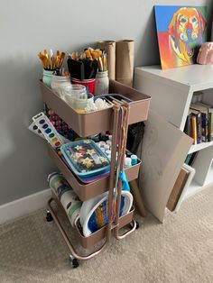 a cart filled with art supplies next to a painting and crafting supplies on wheels