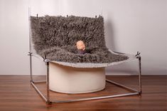 a baby doll is sitting in a chair made out of sheepskin and metal bars