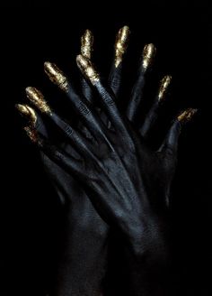 two hands with gold painted nails and black gloves