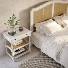 a white bed sitting next to a nightstand with a potted plant on top of it