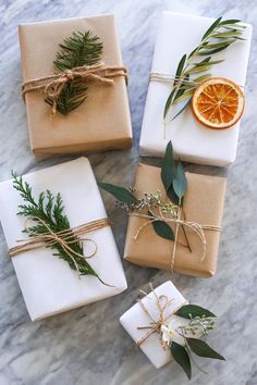 four wrapped presents tied with twine and decorated with greenery, an orange slice and rosemary