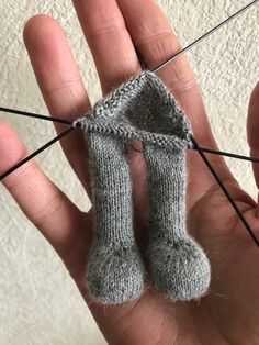 a hand holding a pair of gray knitted mittens with pins sticking out of it