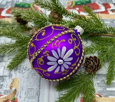 a purple christmas ornament sitting on top of a table next to pine cones