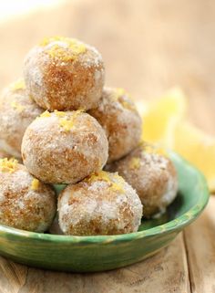 a green bowl filled with donuts covered in powdered sugar and lemon zest