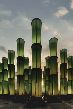 a large group of tall green vases sitting on top of a cement ground next to each other