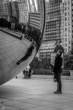 a man standing in front of a large metal object with buildings in the back ground