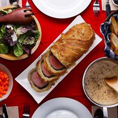 a red table topped with plates and bowls filled with food next to breaded meat