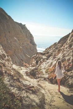 a woman walking down a dirt path next to the ocean