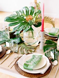 the table is set with green and white plates, silverware, and greenery