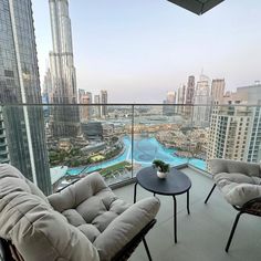 two chairs and a table on top of a balcony overlooking a city with tall buildings