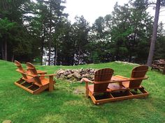 two wooden lawn chairs sitting on top of a lush green field next to a pile of rocks