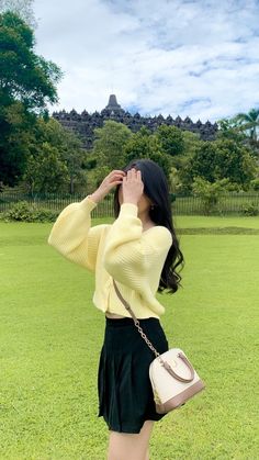 a woman standing on top of a lush green field holding a handbag in her right hand