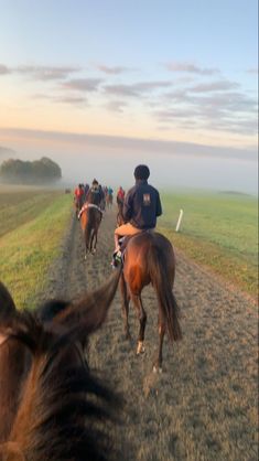 a group of people riding horses down a dirt road in the middle of a field