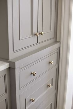 a white cabinet with gold handles and knobs in a room that is painted gray