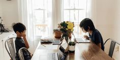 two young boys sitting at a table with laptops and flowers in front of them