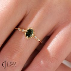 a woman's hand with a gold ring and green stone on top of it