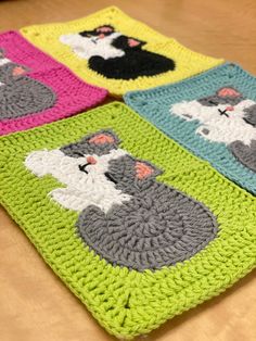 four crocheted coasters with cats on them sitting on a wooden table top