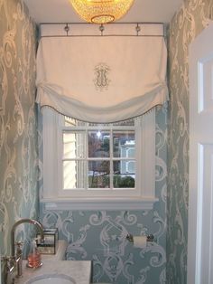 a white toilet sitting under a window next to a sink in a bath room with blue wallpaper