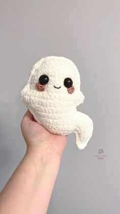 a hand holding a small white crocheted toy with black eyes and a smiling ghost face