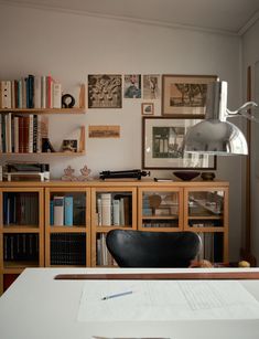 a desk with a lamp, bookshelf and pictures on the wall behind it