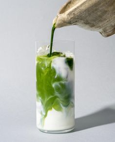 a glass filled with green liquid being poured into it