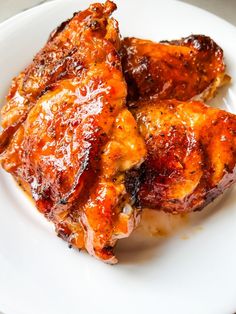 two pieces of chicken sitting on top of a white plate covered in bbq sauce