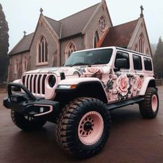 a white jeep with pink roses painted on it's side parked in front of a church