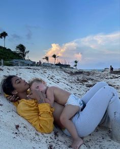 a woman laying on top of a sandy beach next to a baby