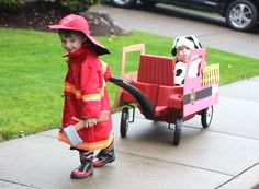 two children in fireman costumes pulling a toy wagon