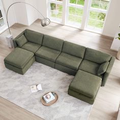 a green sectional sofa sitting on top of a rug in a living room next to a window