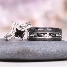 two wedding rings sitting on top of a rock next to each other, with one black and white diamond in the middle