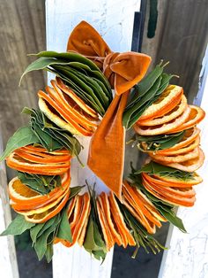 a wreath made out of orange slices and green leaves with a bow hanging on the front door